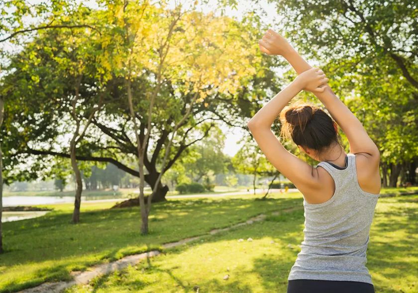 Mulher a praticar exercício físico ao ar livre num parque florido, rodeada por natureza, simbolizando bem-estar e equilíbrio na Primavera.